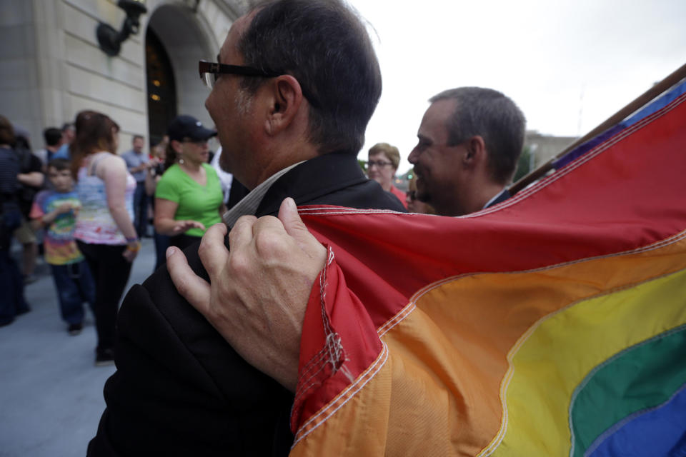 Shon DeArmon, right, puts his arm around his partner James Porter while holding a flag outside the Pulaski County Courthouse in Little Rock, Ark., Monday, May 12, 2014. The state's largest county began issuing gay marriage licenses following a judge's ruling overturning Arkansas' constitutional ban on same-sex marriage. (AP Photo/Danny Johnston)