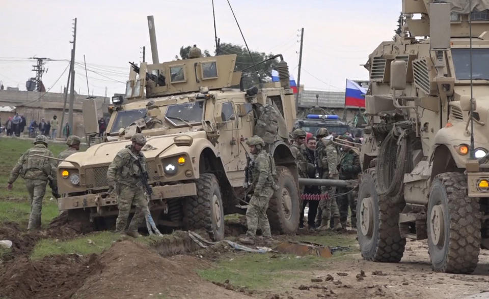 In this frame grab from video, Russian, Syrian and others gather next to an American military convoy stuck in the village of Khirbet Ammu, east of Qamishli city, Syria, Wednesday, Feb. 12, 2020. Syrian media and activists say a Syrian was killed and another wounded in a rare clash between American troops and a group of government supporters in northeast Syria. (AP Photo)