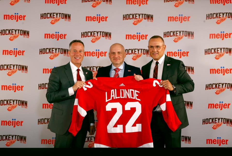 Left to right: Red Wings owner Christopher Ilitch, new Red Wings head coach Derek Lalonde and general manager Steve Yzerman hold up a jersey presented to Lalonde after his introductory news conference at Little Caesars Arena in Detroit on Friday, July 1, 2022.