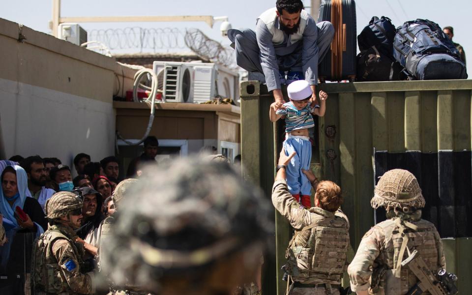 An Afghan man hands his child to a British Paratrooper during the evacuation last week - US Army/AP
