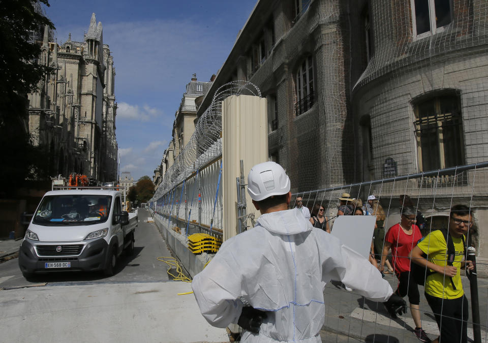 A worker dressed in a white overalls opens the gate on the fence that surround Notre-Dame Cathedral, in Paris, Thursday, Aug. 1, 2019, as the preliminary work begins to repair the fire damage. (AP Photo/Michel Euler)