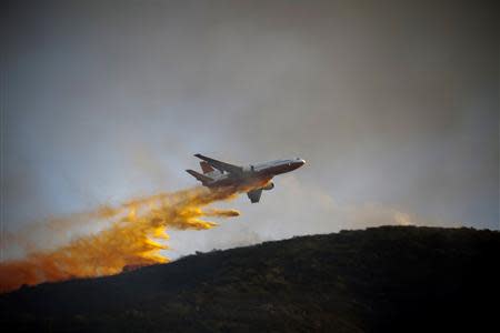 A DC-10 Super Tanker aircraft dumps flame retardant as firefighters battle a blaze in San Marcos, California May 14, 2014. REUTERS/Sam Hodgson