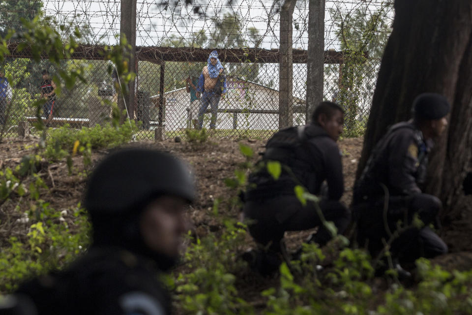 Inmates inside the Pavon Rehabilitation Model Farm watch special task force police taking position on the perimeter after a shooting inside the jail in Fraijanes, Guatemala, Tuesday, May 7, 2019. Cecilio Chacaj of the municipal firefighters says that 10 prisoners were transported to medical facilities with bullet wounds. (AP Photo/Oliver De Ros)