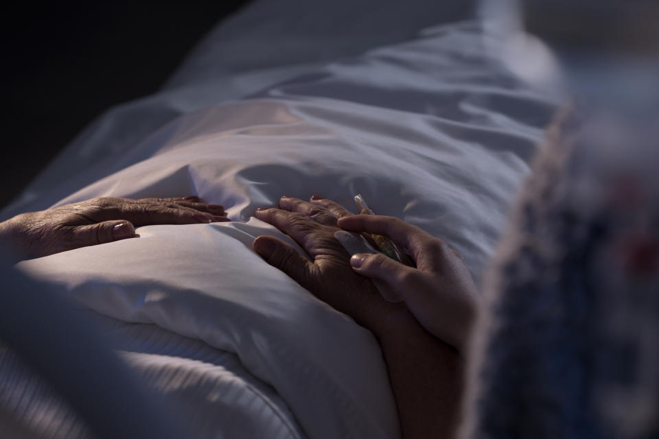 Person resting in bed with another's hand holding theirs in comfort