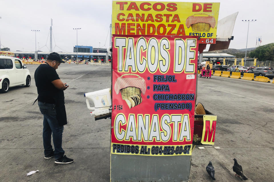 Taco vendor Christian Mendoza works as cars wait to enter the United States at San Diego's San Ysidro border crossing Tuesday, Aug. 25, 2020, in Tijuana, Mexico. A Trump administration crackdown on nonessential travel coming from Mexico amid the coronavirus pandemic has created massive bottlenecks at the border, with drivers reporting waits of up to 10 hours to get into the U.S. (AP Photo/Elliot Spagat)