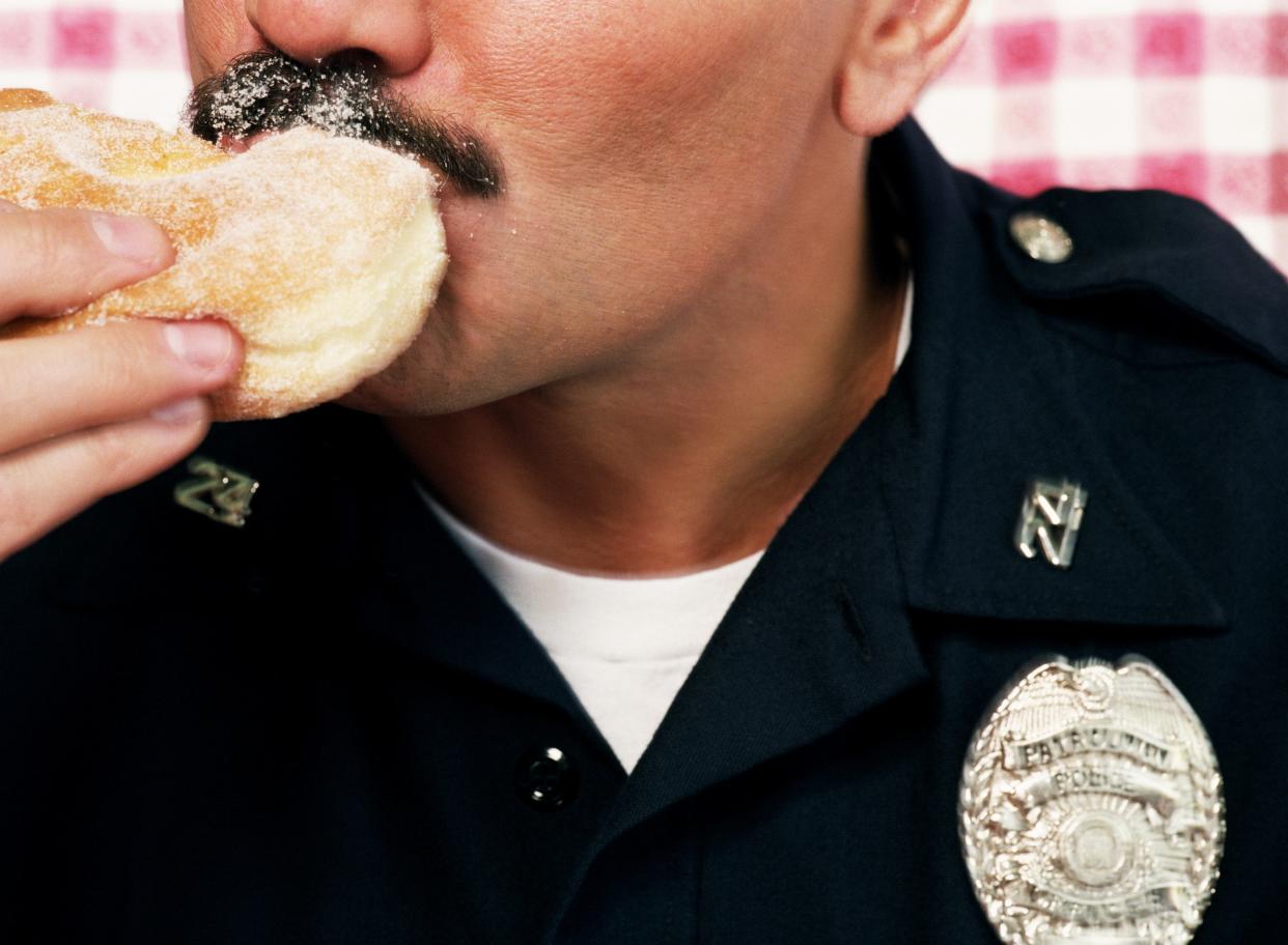 A close up shot of a police officer eating a sugared donut.