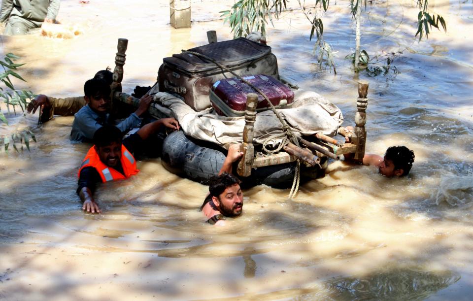 Displaced people float belongings salvaged from flood-hit homes through a flooded area, on the outskirts of Peshawar, Pakistan, Sunday, Aug. 28, 2022.