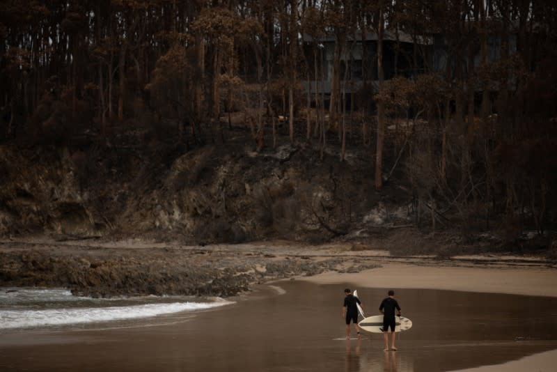 Surfers walk near burnt bushland in Mckenzie beach near Malua Bay