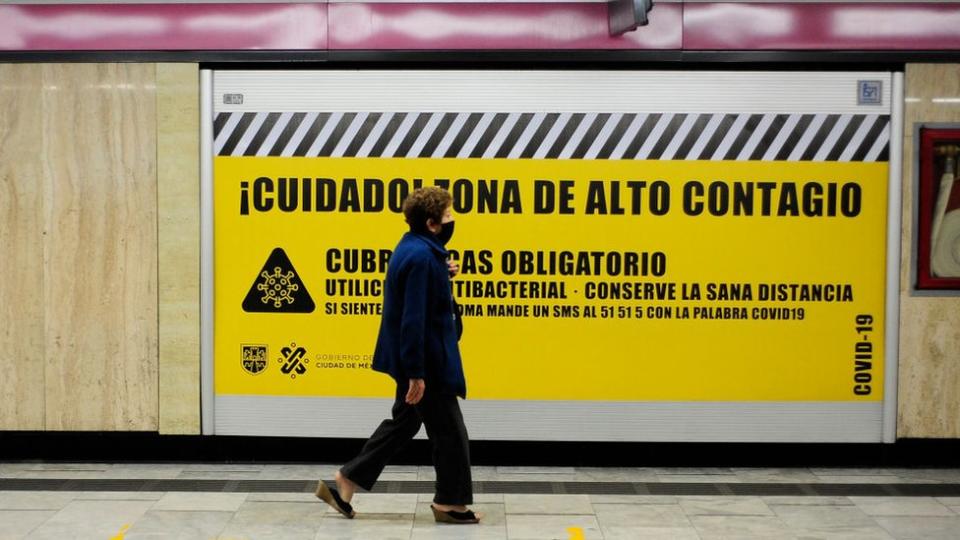 Una mujer con tapabocas pasa frente a un cartel en el metro de la Ciudad de México que aconseja sobre las precauciones contra el coronavirus