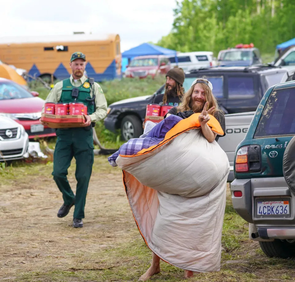 Un miembro de la Familia Arcoíris haciendo la señal de la paz mientras un guardabosques del Servicio Forestal de Estados Unidos ayuda a transportar suministros, el 26 de junio. Los guardabosques y las personas de la Familia Arcoíris dicen que intentan construir una relación de respeto mutuo. A los miembros de la Familia Arcoíris les irrita la presencia policial, pero también afirman que respetan las órdenes de los guardabosques cuando les piden que sigan las reglas.