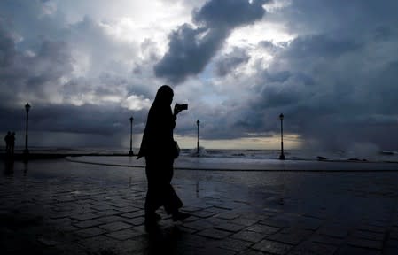 FILE PHOTO: A woman takes photographs with her mobile phone against the backdrop of monsoon clouds at a beach in Kochi