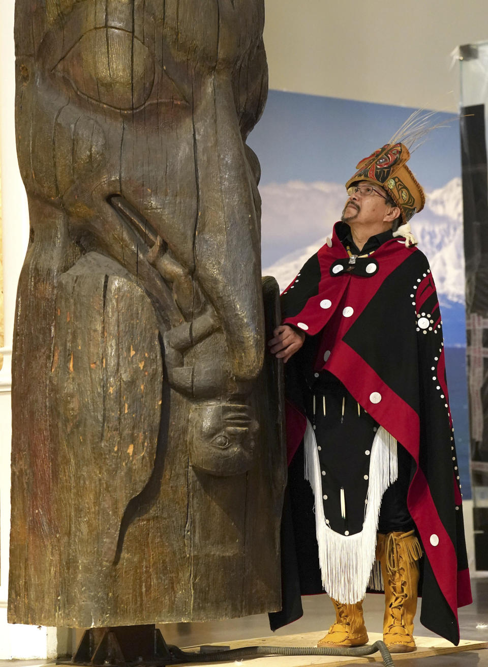 Earl Stephens, who has the Nisga'a cultural name Chief Ni'is Joohl, from the Nisga'a nation, stands besides the 11-metre tall memorial pole, during a visit to the National Museum of Scotland, ahead of its return to what is now British Columbia, in Edinburgh, Monday, Aug. 28, 2023. Members of a Canadian First Nation held a spiritual ceremony on Monday at a Scottish museum to begin the homeward journey of a totem pole stolen almost a century ago. (Andrew Milligan/PA via AP)