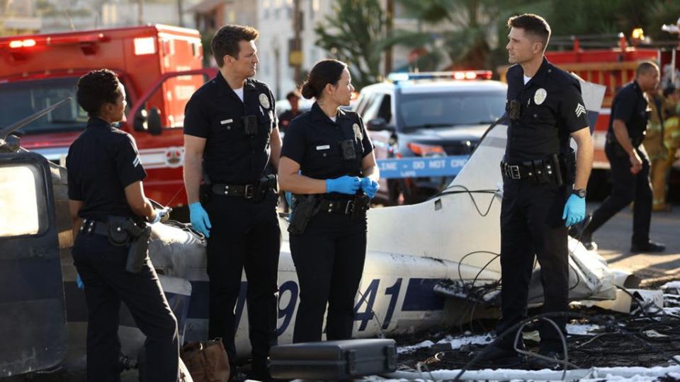 John, Lucy, Tim and Nyla during The Rookie season four episode, Heart Beat. They are standing in the middle of a crime scene where a plane crash has taken place. 