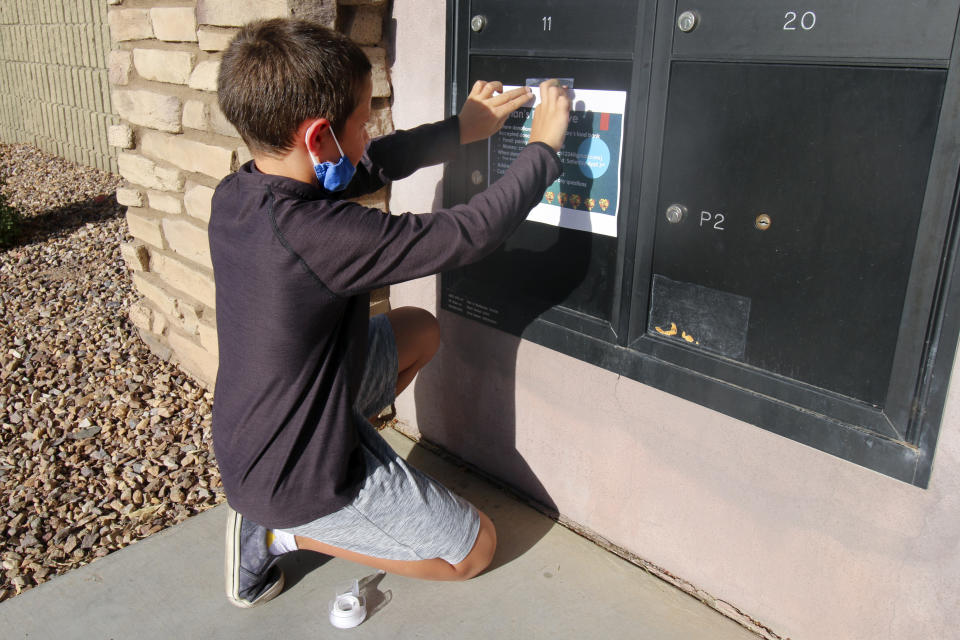 Dylan Pfeifer, 8, tapes up flyers in his neighborhood in Chandler, Ariz. on Thursday, April 1, 2021. The flyers promoted his third food drive since October in response to the coronavirus pandemic. (AP Photo/Cheyanne Mumphrey)