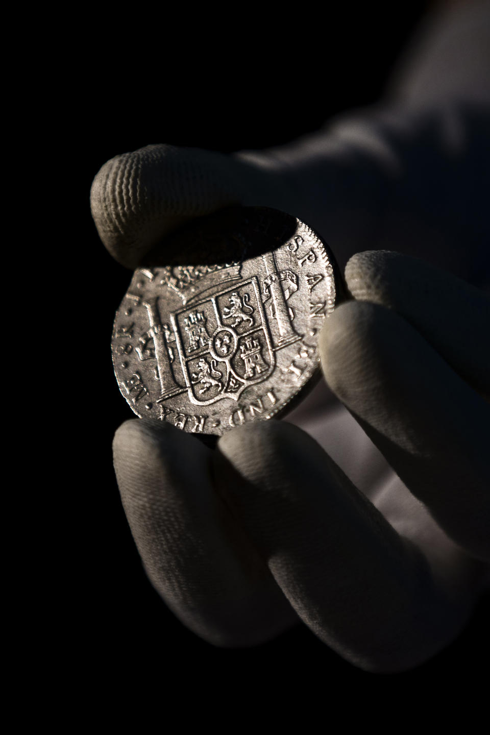 A worker of the ministry holds up for photographers a silver coin from the shipwreck of a 1804 galleon, on its first display to the media at a ministry building, in Madrid, Friday, Nov. 30, 2012. Spanish cultural officials have allowed the first peep at 16 tons (14.5 metric tons) of the shipwreck, 'Nuestra Senora de las Mercedes' a treasure worth an estimated $500 million that a U.S. salvage company gave up after a five-year international ownership dispute. (AP Photo/Daniel Ochoa de Olza)