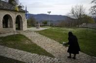 An elderly woman holds flowers as she enters the yard of Agios Georgios church in Monodendri village Zagorochoria, Epirus region, northwestern Greece, on Holy Thursday, April 21, 2022. For the first time in three years, Greeks were able to celebrate Easter without the restrictions made necessary by the coronavirus pandemic. (AP Photo/Thanassis Stavrakis)