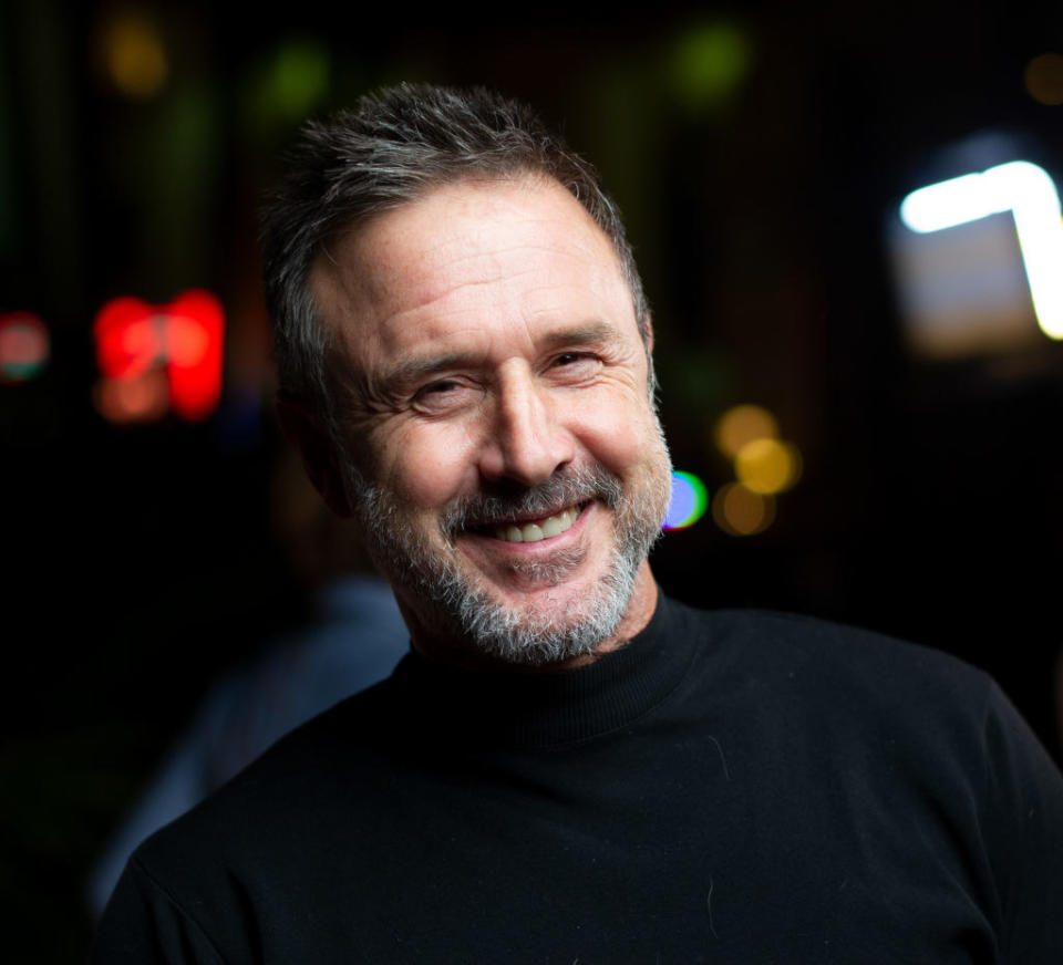 David Arquette smiling and posing on the red carpet in a dark shirt