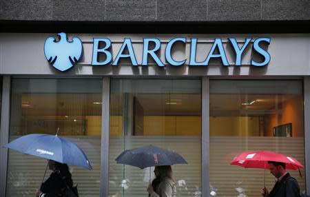 Pedestrians shelter under umbrellas as they walk past a Barclays branch in central London May 8, 2014. REUTERS/Stefan Wermuth