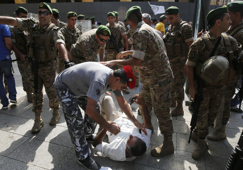 Lebanese army soldiers, help their retired comrade who fall down while he was running try to enter the parliament building, where lawmakers and ministers are discussing the draft 2019 state budget, in Beirut, Lebanon, Friday, July 19, 2019. The budget is aimed at averting a financial crisis in heavily indebted Lebanon. But it was met with criticism for failing to address structural problems. Instead, the budget mostly cuts public spending and raises taxes. (AP Photo/Hussein Malla)