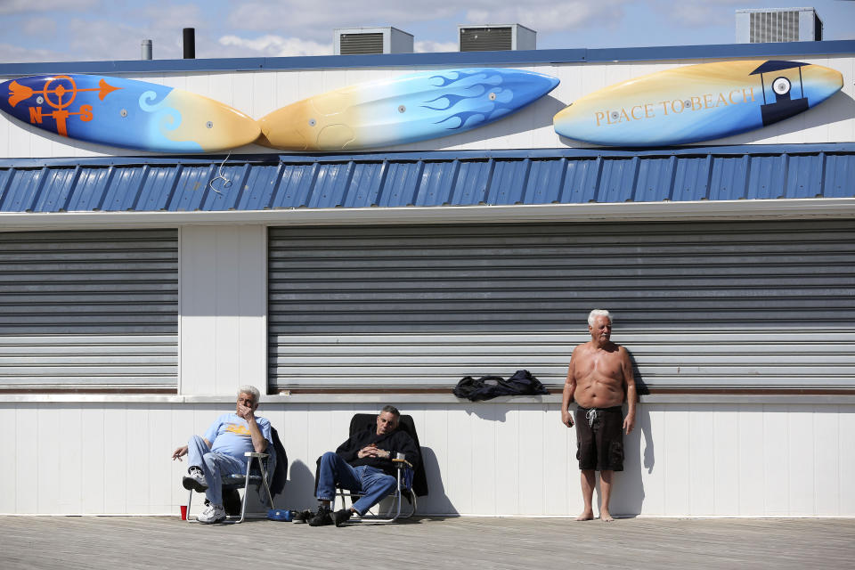 In a Saturday March 30, 2013, photo men sunbathe in front of a closed business on the boardwalk of New York's Coney Island. Despite making the traditional Palm Sunday opening, many of the seasonal businesses at Coney Island are still reeling from the aftermath of Superstorm Sandy. (AP Photo/Mary Altaffer)