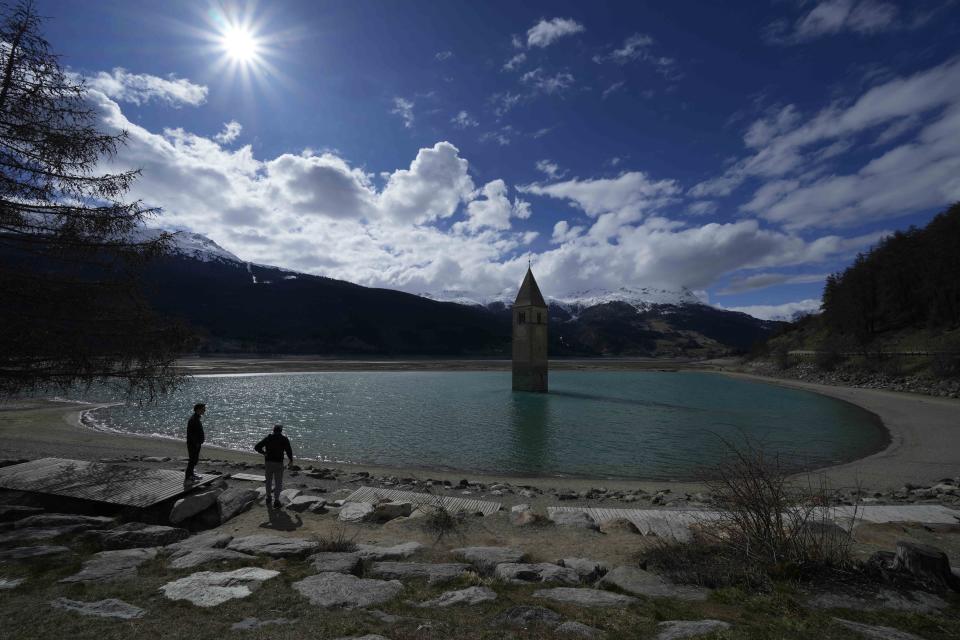 Two visitors stand near the Resia artificial lake, in Curon Venosta, northern Italy, Monday, April 17, 2023. The ancient bell tower of the now-submerged village of Curon Venosta stands taller than usual in the lake.(AP Photo/Luca Bruno)