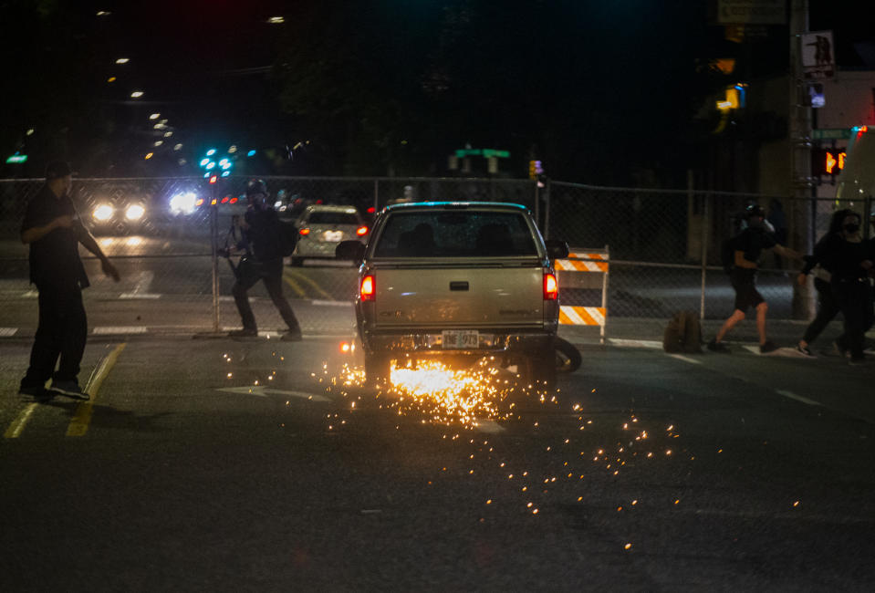 A driver in a pickup truck accelerates towards the crowd, hitting and dragging a motorcycle during a protest in Portland, Ore., on Tuesday, Aug. 4, 2020. A riot was declared early Wednesday during demonstrations in Portland after authorities said people set fires and barricaded public roadways.(Dave Killen /The Oregonian via AP)