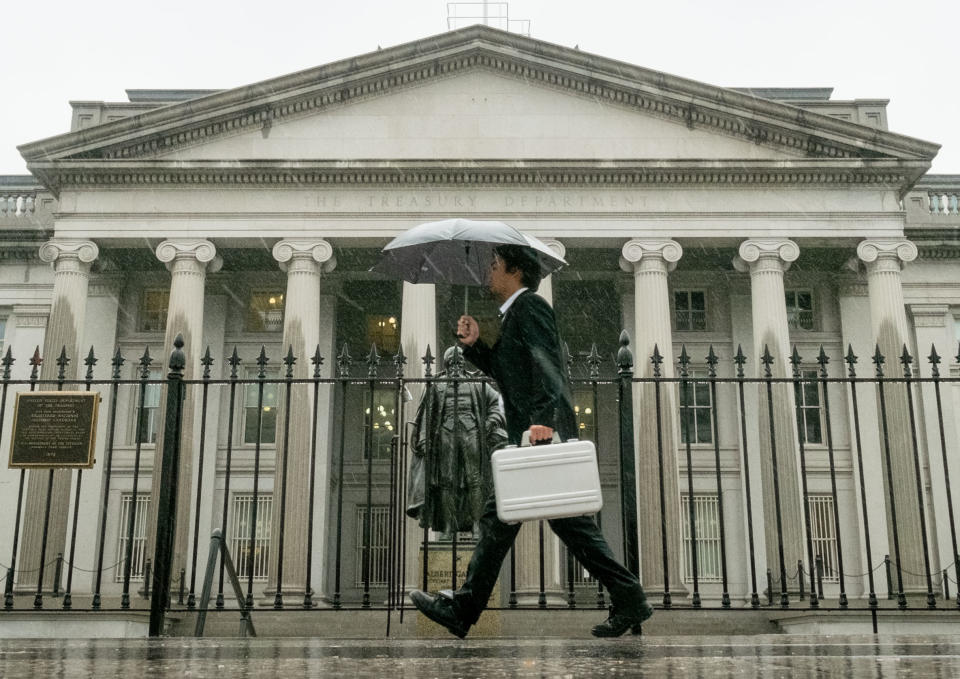 In this Thursday, Oct. 10, 2013 photo, a pedestrian walks past the U.S. Treasury Building in Washington on a rainy day. The national debt actually reached the limit in May 2013. Since then, Treasury Secretary Jacob Lew has made accounting moves to continue financing the government without further borrowing. But Lew says those measures will be exhausted by Thursday, Oct. 17, 2013. The government will then have to pay its bills from its cash on hand — an estimated $30 billion — and tax revenue. (AP Photo/J. David Ake)