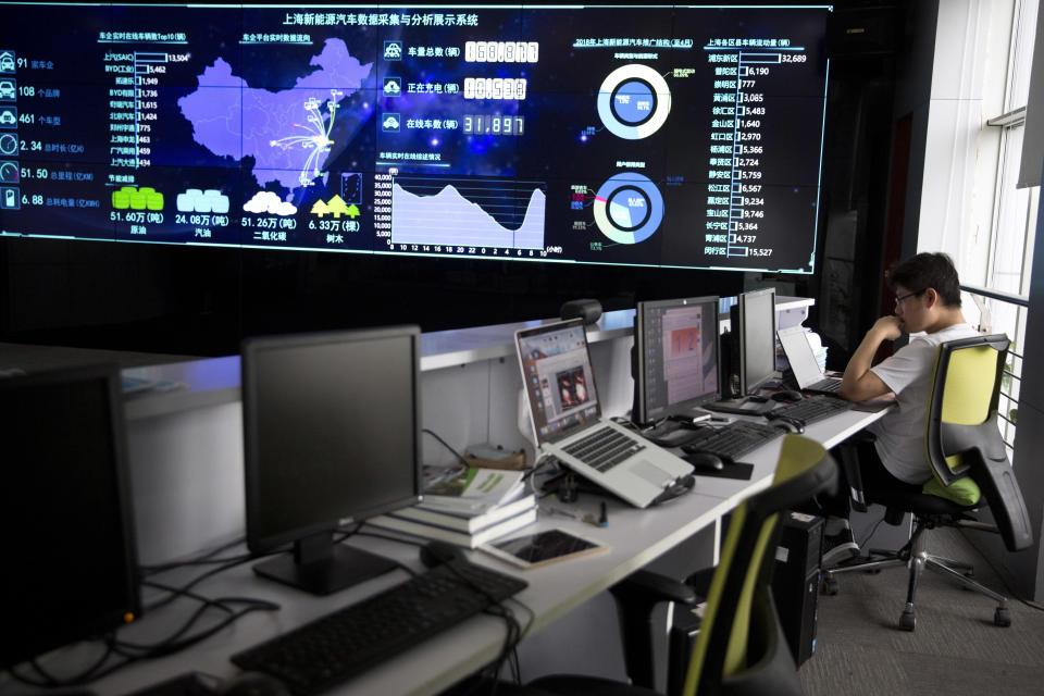 In this Friday, June 22, 2018, photo, a staff member looks at a laptop near a screen displaying live data from vehicles at the Shanghai Electric Vehicle Public Data Collecting, Monitoring and Research Center in Shanghai. According to specifications published in 2016, every electric vehicle in China transmits data from the car's sensors back to the manufacturer. From there, automakers send 61 data points, including location and details about battery and engine function to local centers like this one in Shanghai. (AP Photo/Ng Han Guan)