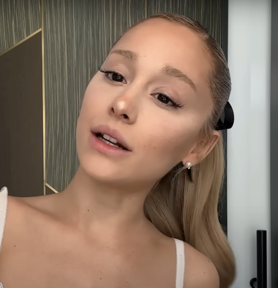 Ariana Grande posing with a subtle smile, minimal makeup, and hair in a high ponytail