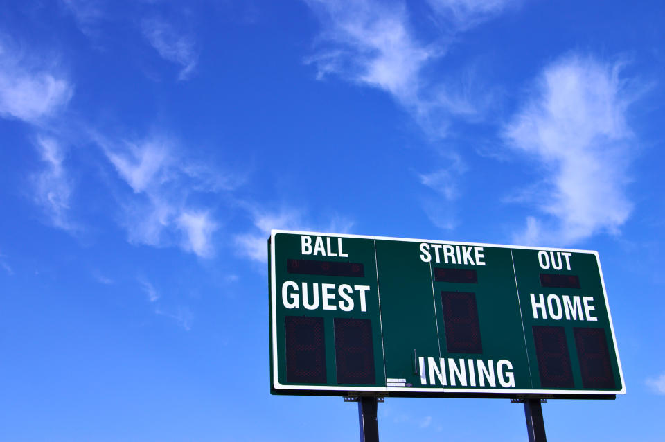 A baseball scoreboard, showing no scores for either team, against a mostly blue sky.