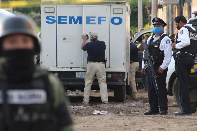 Police officers stand guard as a man closes the door of the coroner's vehicle outside a drug rehabilitation facility where assailants killed several people, according to Guanajuato state police, in Irapuato