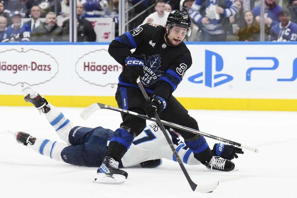 Toronto Maple Leafs forward Auston Matthews (34) protects the puck from a sliding Winnipeg Jets forward Nikolaj Ehlers (27) during overtime of an NHL hockey game Wednesday, Jan. 24, 2024, in Toronto. (Nathan Denette/The Canadian Press via AP)