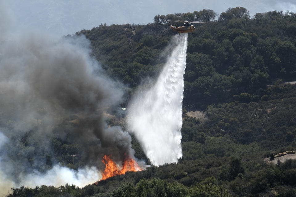 A helicopter drops water on a wildfire Wednesday, Oct. 13, 2021, in Goleta, Calif. A wildfire raging through Southern California coastal mountains threatened ranches and rural homes and kept a major highway shut down Wednesday as the fire-scarred state faced a new round of dry winds that raise risk of infernos. (AP Photo/Ringo H.W. Chiu)