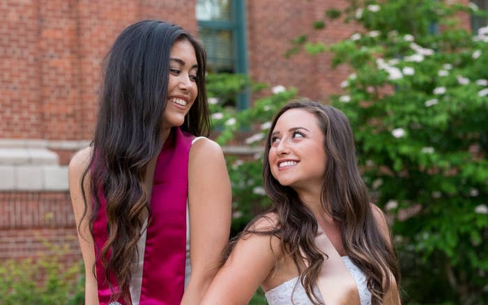 Two women smiling at each other while standing outside, dressed in elegant attire. Names of individuals are unknown