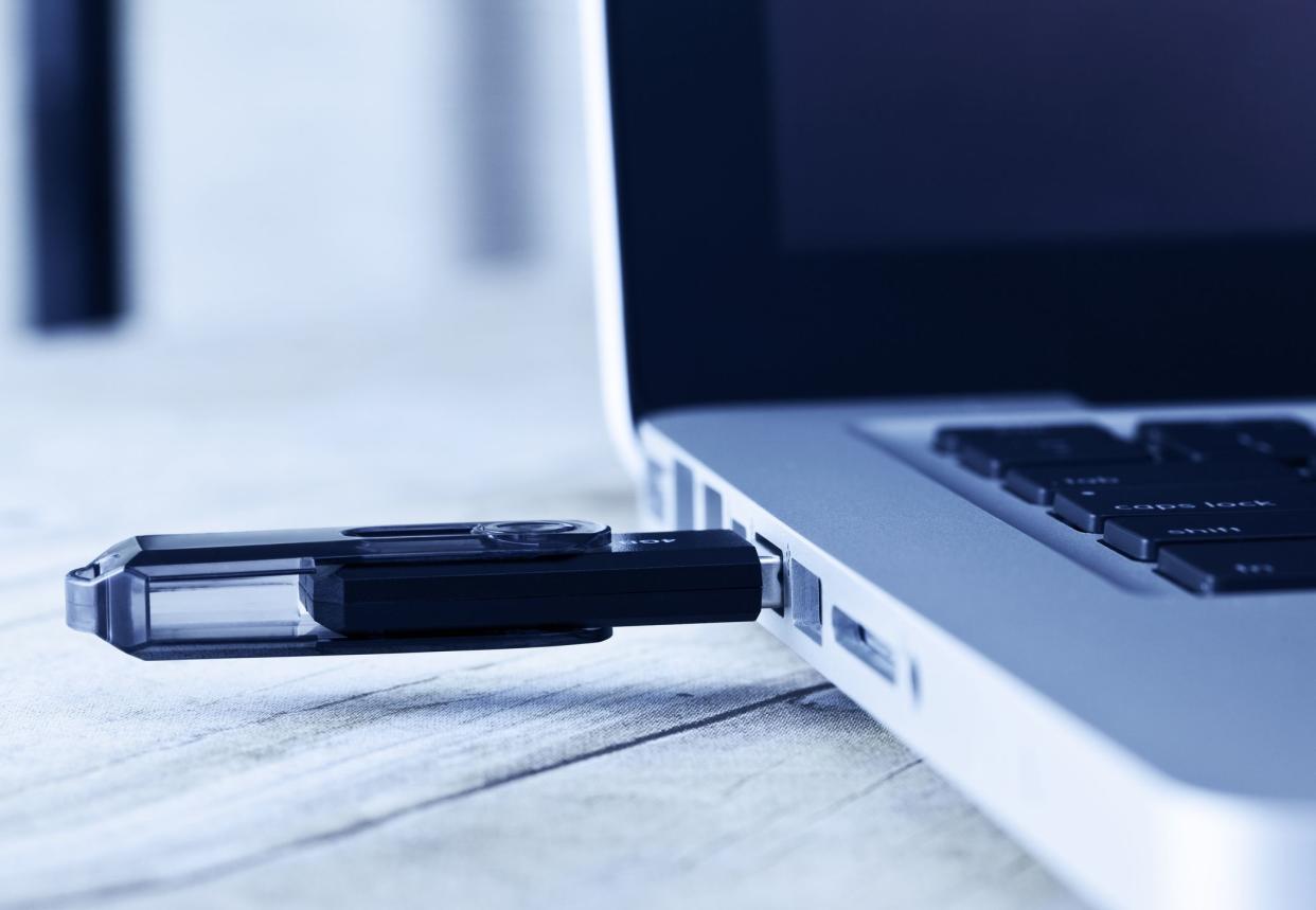 Closeup of a USB flash drive connected to the side of a laptop with cool blue coloring of image, a blurred background