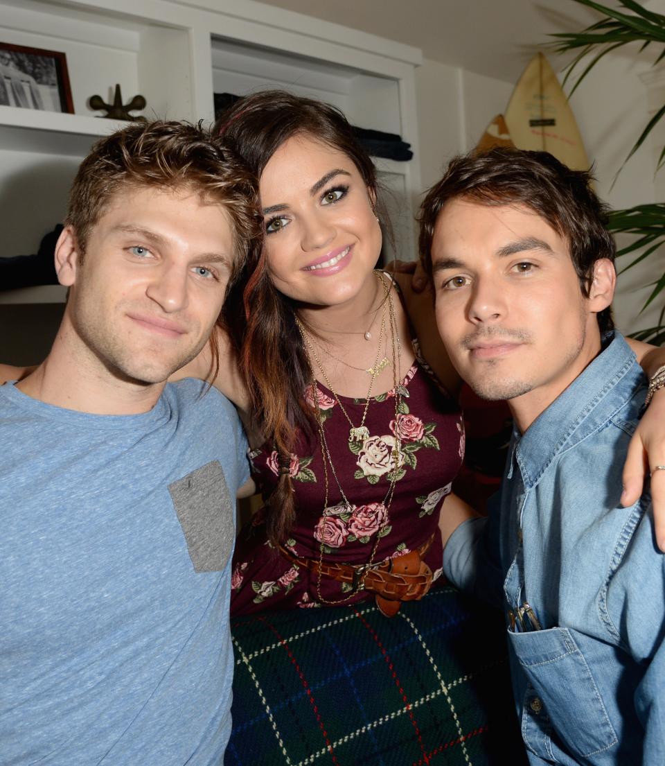 Keegan Allen, Lucy Hale, and Tyler Blackburn smile while seated closely with their arms around each other in a casual setting