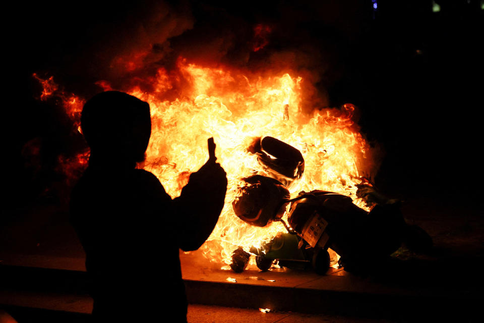 A person stands near a burning scooter, as protesters gather at the Place de la République during a demonstration over pension reform in Paris, on March 21, 2023. 