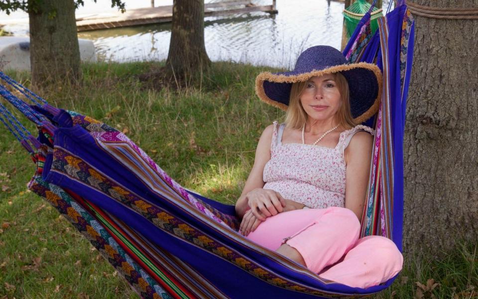 Julia Stephenson, who is wearing pink trousers and wide-brimmed hat, sits in a hammock by a river - Eyevine/David Sandison