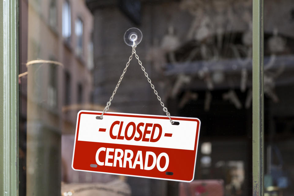 Close-up on a red Closed sign in a window with written in it in Spanish and English.