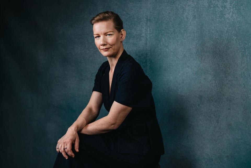 Sandra Hüller sits on a chair hands crossed over her knees for a portrait.