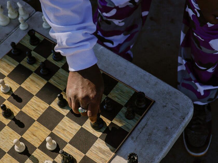 A hand moves a chess piece on a board, as seen from above. 