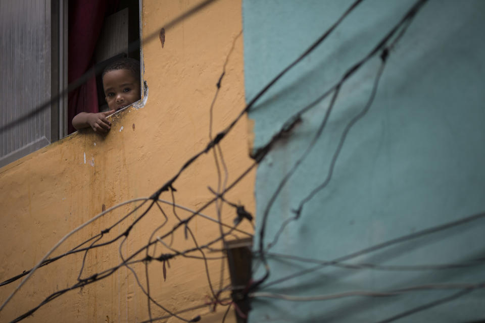 A young resident looks out from his window as military police officers patrol during an operation in the Mare slum complex, ahead of its "pacification," in Rio de Janeiro, Brazil, Tuesday, March 25, 2014. Elite federal police and army troops will be sent to the city to help quell a wave of violence in so-called "pacified" slums. Recent attacks on police bases in the favelas is raising concerns about an ambitious security program that began in 2008, in part to secure the city ahead of this year's World Cup and the 2016 Olympics. (AP Photo/Felipe Dana)