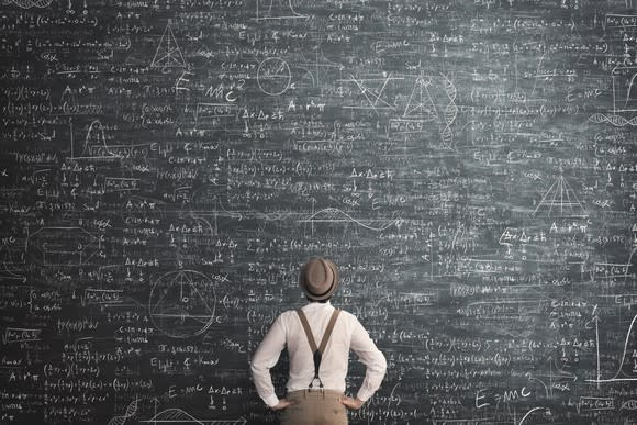 Man standing in front of a chalkboard with equations and charts on it.