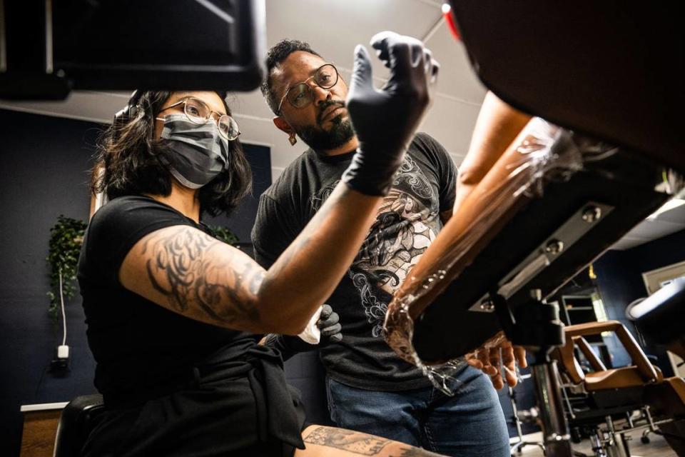 David Ramsés Cabral, copropietario del estudio de tatuajes Ghost Ink de Sacramento, habla con la artista Jo Mean sobre cómo colocarse mejor mientras trabaja en un tatuaje, el martes. Hector Amezcua/hamezcua@sacbee.com