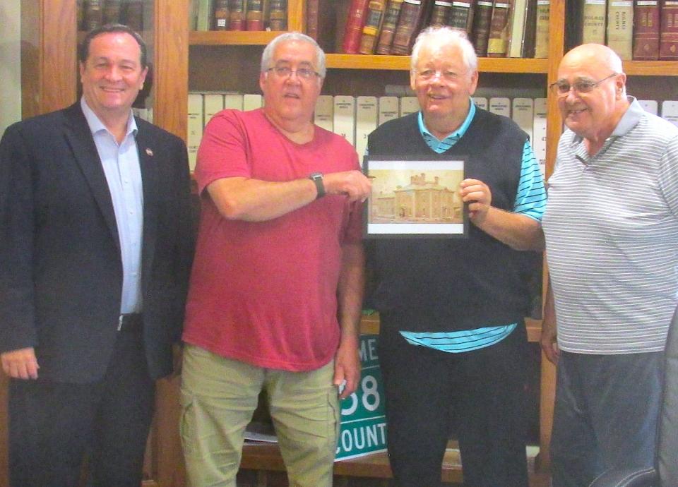 Millersburg resident David Weiss presents a photo of the old Holmes County Sheriff's Office to Holmes County Commissioners Dave Hall (at left), Joe Miller and Ray Eyler.