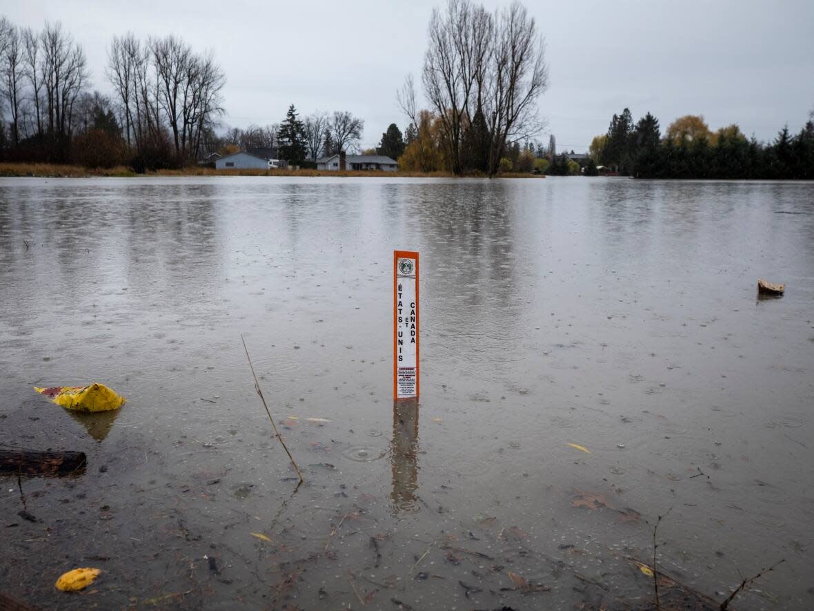 An international border marker between the U.S. and Canada is pictured submerged in water in the Sumas Prairie flood zone in Abbotsford, B.C. on Nov. 30, 2021. According to Ben Parfitt, policy analyst at the Canadian Centre for Policy Alternatives, understaffing could lead to an inability to effectively communicate timely flood risk warnings. (Ben Nelms/CBC - image credit)