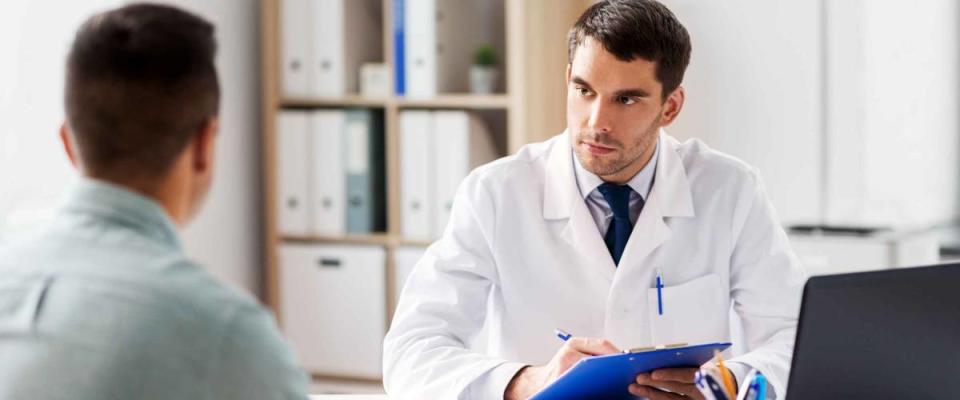 medicine, healthcare and people concept - doctor with clipboard talking to male patient at medical office in hospital