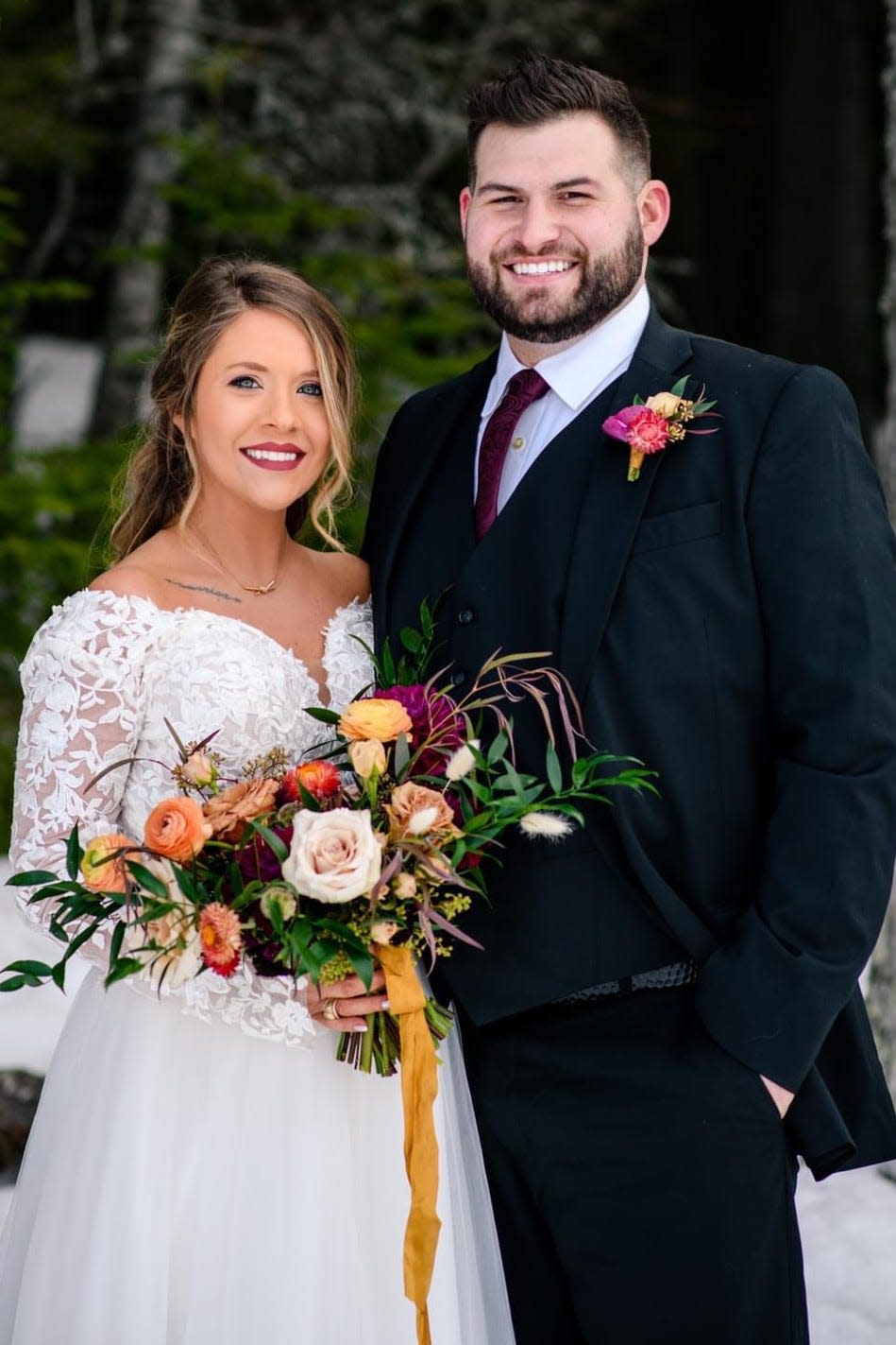 A bride and groom standing near pine trees and snow