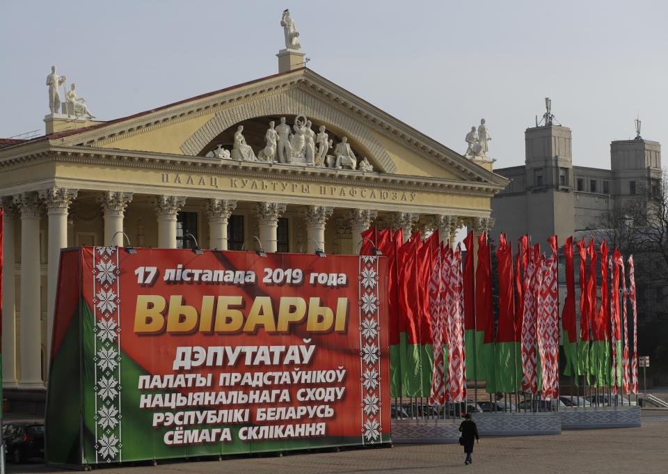 In this photo taken on Wednesday, Nov. 13, 2019, a woman walks past a huge election banner and Belarus national flags in Minsk, Belarus, ahead of the parliamentary election to be held on Sunday. (AP Photo/Sergei Grits)