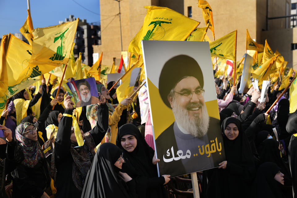 Hezbollah supporters hold a portrait of Hezbollah leader Sayyed Hassan Nasrallah with Arabic words read: "We will stay with you," during an election campaign, in the southern suburb of Beirut, Lebanon, Tuesday, May 10, 2022. Despite a devastating economic collapse and multiple other crises gripping Lebanon, the culmination of decades of corruption and mismanagement, the deeply divisive issue of Hezbollah's weapons has been at the center of Sunday's vote for a new 128-member parliament. (AP Photo/Hussein Malla)